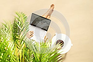 Woman freelancer with laptop sitting under coconut palm tree  branches. Female eating royal dates fruit from a bowl. Summer sand