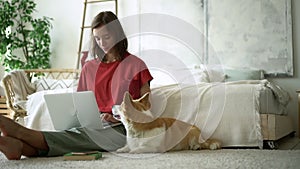 Woman freelancer sit on floor and work type at laptop with corgi Avki. female browse internet online