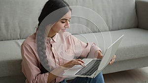 Woman freelancer smiling Arabian Indian girl on floor businesswoman working from home typing message on laptop studying