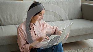 Woman freelancer smiling Arabian Indian girl on floor businesswoman working from home typing message on laptop studying