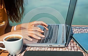 Woman freelancer using laptop computer on beach by sea. hands typing text on keyboard, searching information.