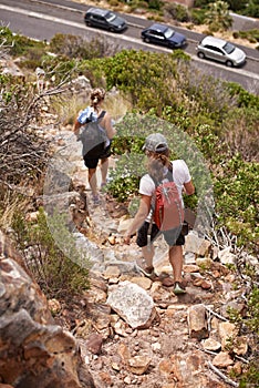 Woman, friends and hiking with backpack on mountain, rocky trail or outdoor path in nature. Rear view of female person