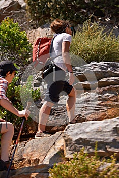 Woman, friends and hiking up mountain with backpack on rocky trail or outdoor path in nature. Active female person or