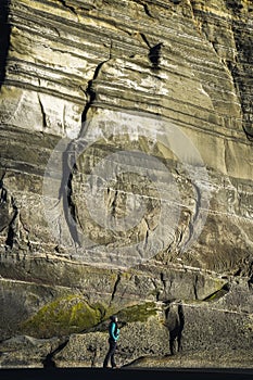 Woman in front of big cliff, a rock formation wall by the beach