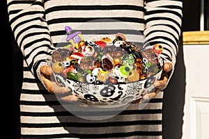 Woman at the front door offering Halloween candies on a nice bowl.