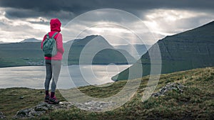 Woman in front of lightbeams through clouds in sky on Faroe Islands