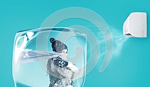 Woman frozen in an ice cube under the air jet of an air conditioner on cyan background