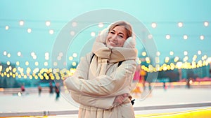 Woman frozen on winter street hugging himself dressed warm winter clothes and earmuffs standing outside on city street