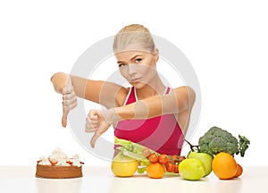 Woman with fruits showing thumbs down to cake