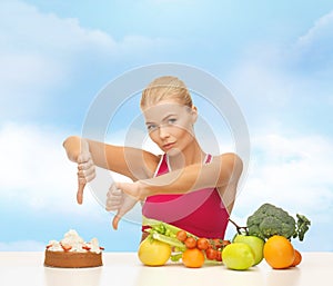 Woman with fruits showing thumbs down to cake