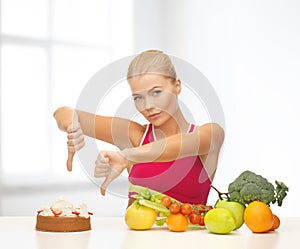 Woman with fruits showing thumbs down to cake