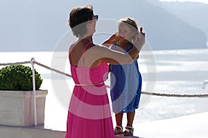 Woman with fuchsia dress plays with her little daughter on Oia Scenery as a background in Santorini