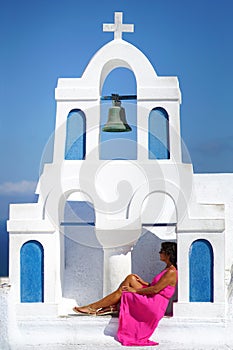 Woman with fuchsia dress sits in the bell tower of a small church in Oia in Santorini