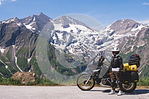 Woman in full biker outfit, copy space. Touring motorcycle with big bags. The snowy peaks of the Sonnenwelleck and Hohe Dock