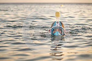 Woman in full face snorkeling mask in sea near coral reef