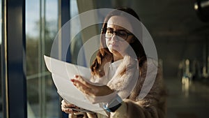 The woman in the fur coat at the airport at the window in the last light of the sun looks on the runway in anticipation