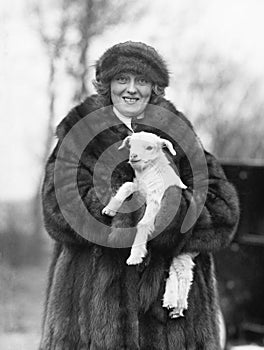 Woman in a fur coat and hat holding a small baby lamb in her arms