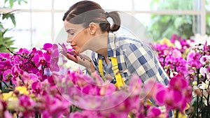 Woman in the garden of flowers, touches an orchid and smiling