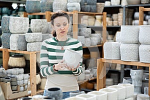 Woman in garden goods store chooses flower pot, studies assortment, admires ceramic products