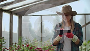 Woman gardener in a hat looking for flowers. A modern Florist uses a tablet computer to analyze the yield of flowers.