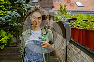 Woman gardener holding a hosepipe for watering plants in garden center and looks camera