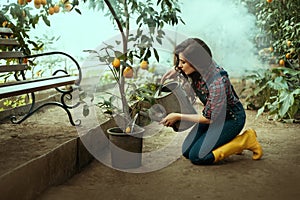 Woman gardener sits on her lap, pouring lemon with water from a watering can. girl in work clothes, plaid shirt, denim