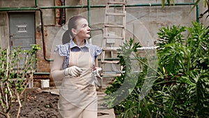 Woman gardener is walking in greenhouse satisfied with her work and putting off her gloves.