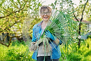 Woman in gardening gloves with white daffodil bush plant and shovel, female looking at camera