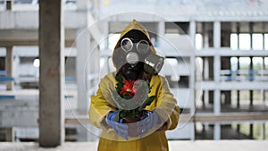 woman in gas mask and yellow overalls found flower, life was born, shows and holds it out to camera. Post apocalypse