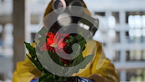 woman in gas mask and yellow overalls found flower, life was born, shows and holds it out to camera. Post apocalypse