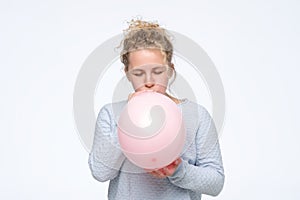 Woman in gblue sweateris blowing pink balloon preparing for birthday party