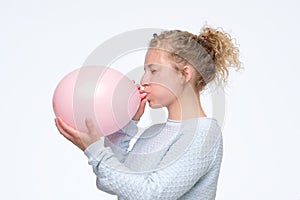 Woman in gblue sweateris blowing pink balloon preparing for birthday party