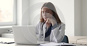 Woman general practitioner in white coat working sit at workplace