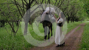 Woman gently petting horse in peaceful woodland setting. Serene moment as woman walks and bonds with horse among trees.