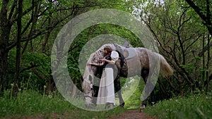 Woman gently petting horse in peaceful woodland setting. Serene moment as woman walks and bonds with horse among trees.