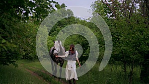 Woman gently petting horse in peaceful woodland setting. Serene moment as woman walks and bonds with horse among trees.