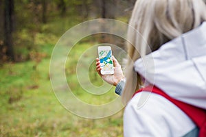 Woman geocaching in forest and using map app on smartphone