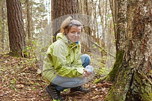 A woman geocaching. Women in woods find geocache container.