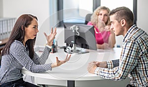 Woman gesticulates to a man angry over disagreement with demale mediator sitting behind the table in the background