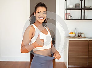 woman gesturing thumbs up pulling waist of fitness pants indoors