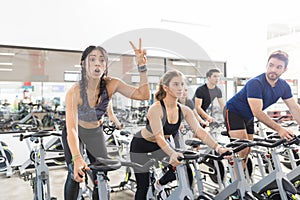 Woman Gesturing Victory While Exercising On Spinning Bike In Gym