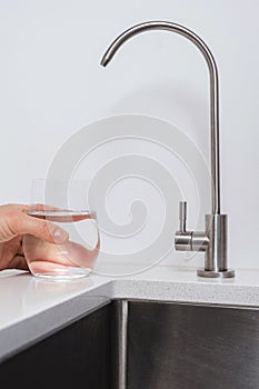 Woman get filtered water from stainless faucet into a glass