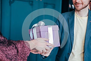 Woman get gift box with gray silver ribbon from young attracrive man on blue background