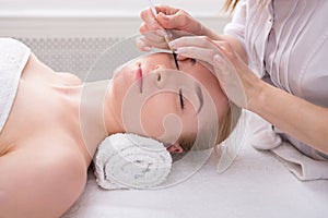 Woman gets eyelashes tinting by beautician at spa