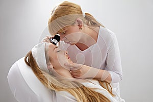 Woman gets professional skin exam at doctor& x27;s office. Dermatologist or cosmetology specialist uses magnifying glass