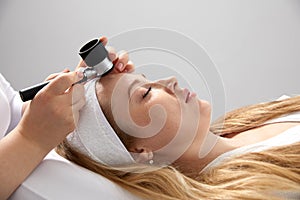 Woman gets professional skin exam at doctor& x27;s office. Dermatologist or cosmetology specialist uses magnifying glass