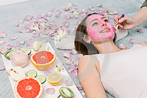 Woman getting facial care by beautician at spa salon, side view, close-up. Young beautiful girl receiving pink facial