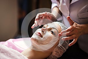 woman getting facial care peeling mask by beautician at spa salon