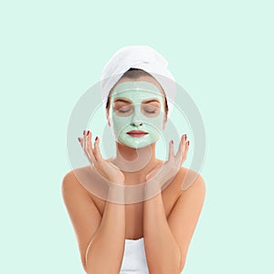 Woman is getting facial clay mask on pastel green background. Beauty and spa