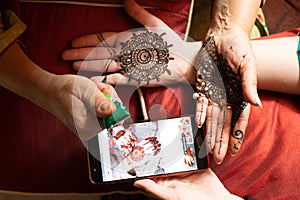 Woman getting a henna tattoo mehendi design copied from phone onto her hand for the bride bridesmaid shaadi event or a